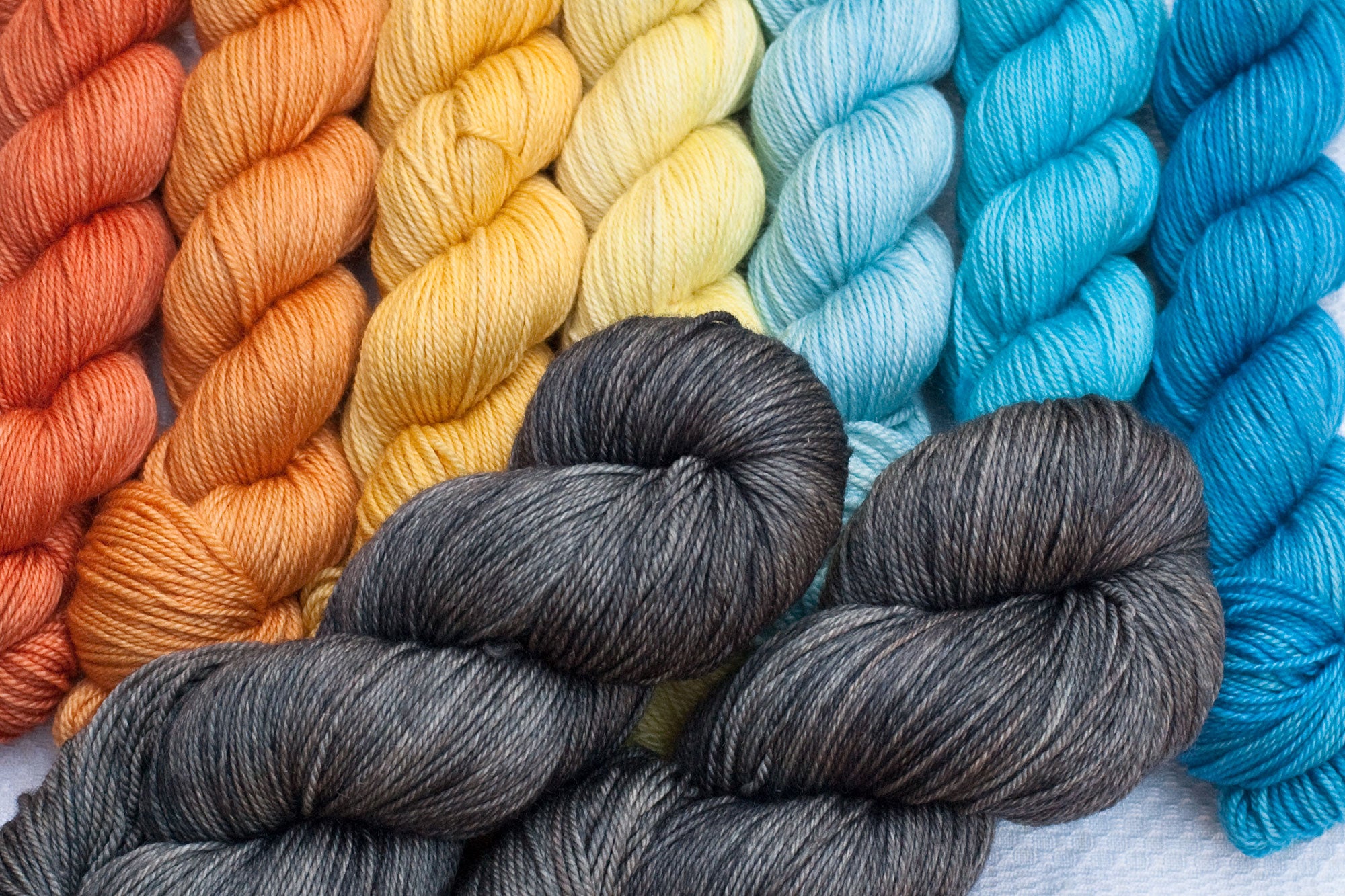 mountain musings mkal hand-dyed yarn set: gradient from orange through yellow and blue, paired with medium grey full skeins