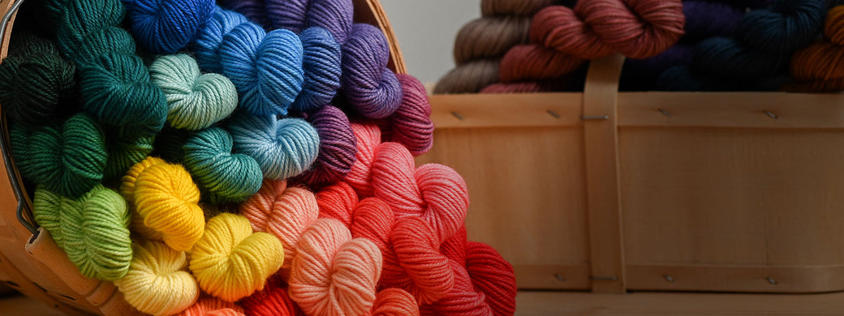 A wooden basket on its side with a rainbow of mini-skeins of yarn tumbling out of it