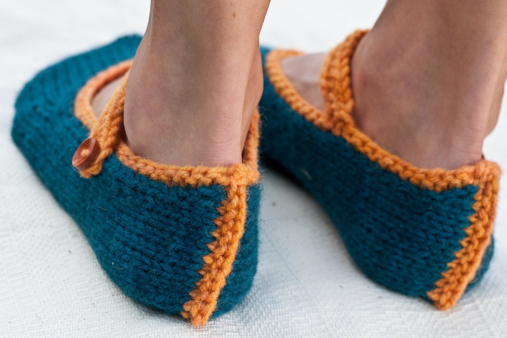 woman's feet wearing hand-knit slippers shown from back and focused on heel seam detail in contrast colour