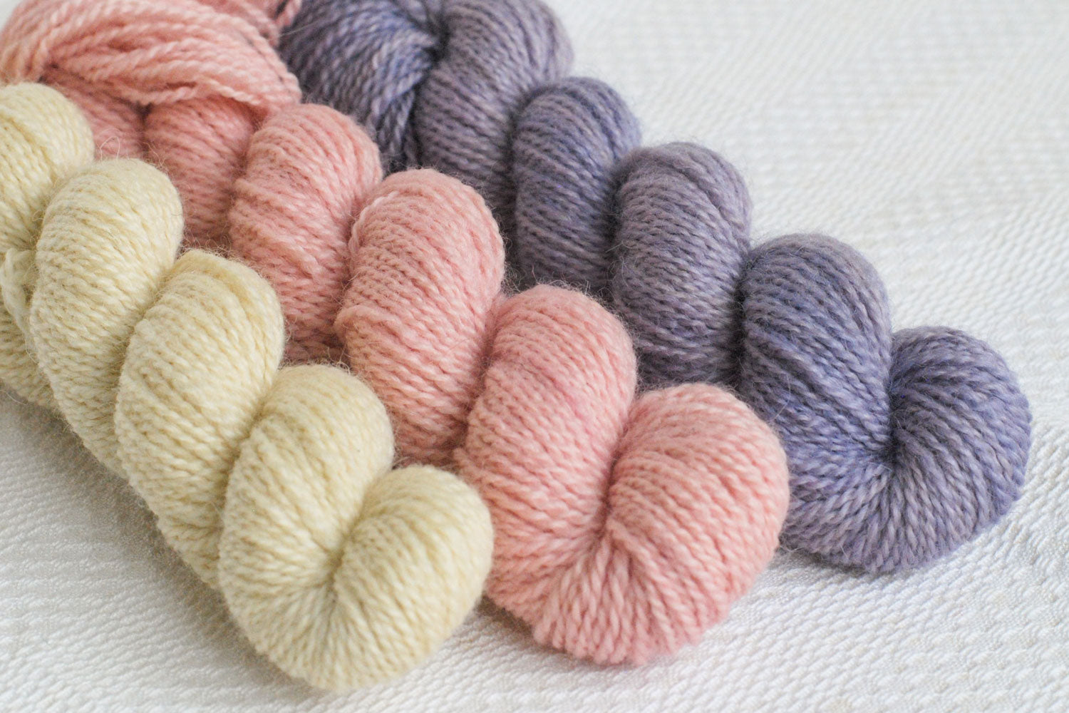 Set of three hand-dyed mini-skeins in natural, light pink, and light purple