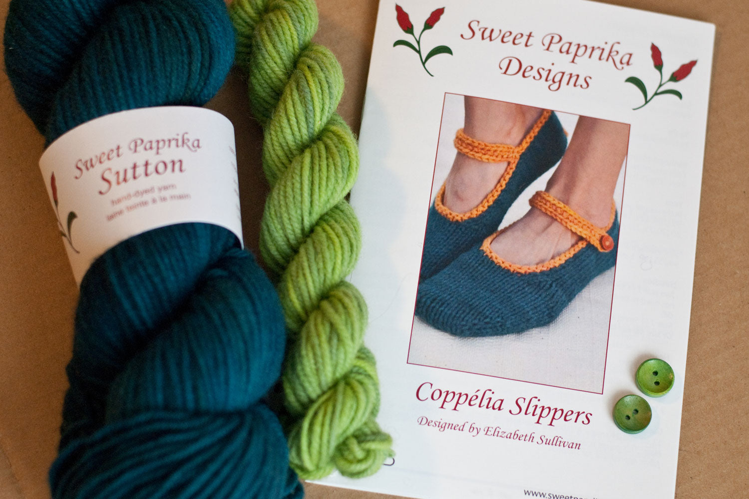 Kit components: knitting pattern, bulky yarn in teal and bright green, green buttons