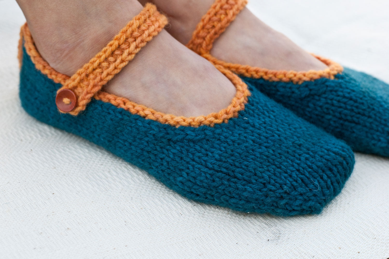 woman's feet wearing sporty hand-knit slippers in dark teal with an orange strap and button